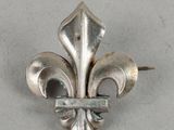 a close up of a metal fleur de lis brooch on a white surface