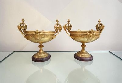 two gold vases on a glass table with a white wall in the background