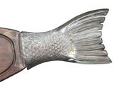 a silver fish shaped object on a wooden plate