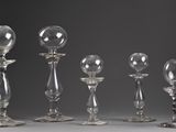 six clear glass candlesticks are lined up against a gray background
