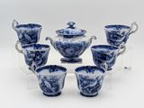 six tasses à thé bleues et blanches avec leurs soucoupes, posées sur un présentoir transparent