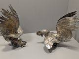 paire de figurines anciennes en argent plaqué représentant des coqs, posées sur une table blanche