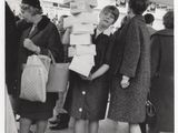 photo en noir et blanc d'un groupe de femmes debout autour d'une pile de cartons