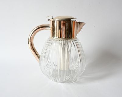 a glass pitcher with a metal handle on a white surface
