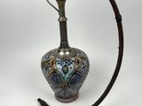 un vieux vase argenté et bleu muni d'une poignée en bois, sur fond blanc