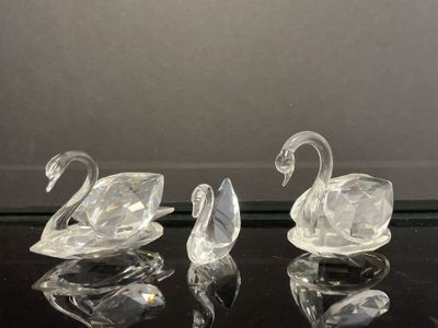 trois figurines de cygnes en verre transparent posées sur une table noire