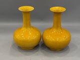 pair of yellow vases sitting on top of a white table