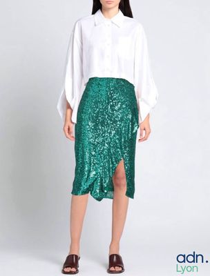 une femme vêtue d'une chemise blanche et d'une jupe verte à paillettes
