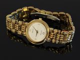 a gold bracelet watch with a white face on a black surface