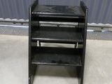 a black shelf with three shelves on it in front of a metal wall