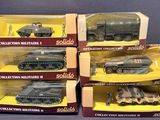 six véhicules militaires emballés dans des cartons, posés sur une surface grise