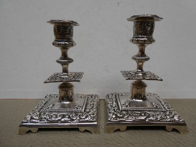 une paire de bougeoirs plaqués argent posés sur un socle, sur une table