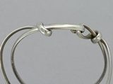 silver bracelet with a knot around the end of it on a white surface