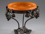 an orange glass bowl on a metal stand with flowers and leaves