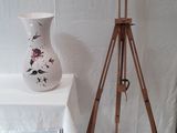 une table blanche sur laquelle se trouve un vase blanc, à côté d'un trépied