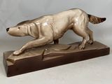 statue d'un chien en train de courir, posée sur un socle en bois, sur fond blanc