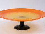 un plat à gâteau en verre orange posé sur un socle noir