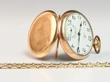 une montre de poche en or avec une chaîne, posée sur une surface blanche