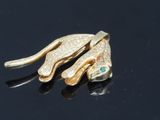 two gold snake brooches with emerald eyes on a black surface