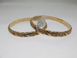 two gold bang bracelets with engraved designs on them on a white surface