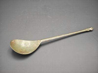 an antique silver spoon with a long handle on a gray surface