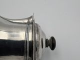 a silver coffee pot on a wooden handle on a table