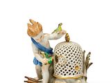 une figurine représentant un garçon avec un oiseau et une cage à oiseaux