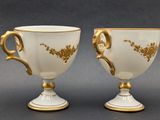 two white and gold coffee cups with gold decoration on them