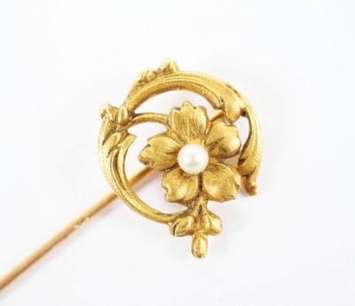 a close up of a gold brooch with a pearl in the center