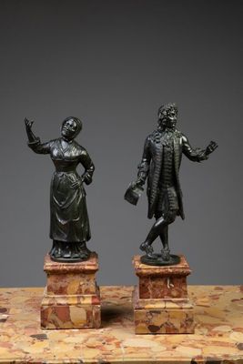 deux statues en bronze représentant un homme et une femme, posées sur des socles en marbre
