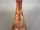 a red and gold vase sitting on a white surface