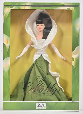 La poupée se trouve dans une boîte, vêtue d'une robe verte et d'un voile blanc.