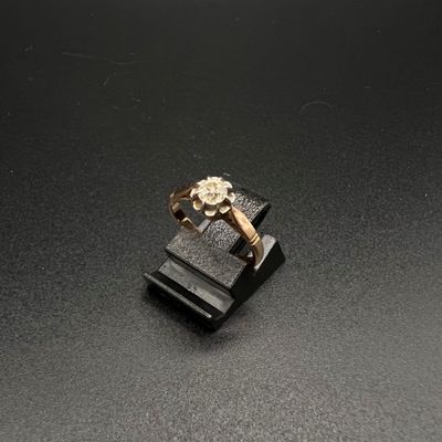 une image représentant une bague en or sertie d'un diamant, posée sur un socle noir