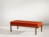 un banc en velours orange avec des pieds en bois, posé sur un sol blanc