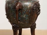 a bronze vase sitting on a wooden stand on a table