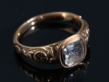 un gros plan d'une bague en or sertie d'une pierre transparente, posée sur une surface noire