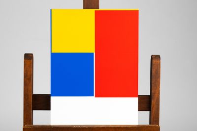 un chevalet en bois sur lequel est posé un tableau et un bloc de couleur rouge, jaune et bleu