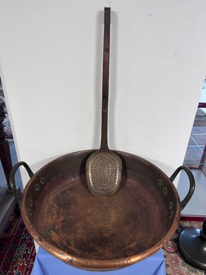 une grande casserole en cuivre sur laquelle est posée une louche