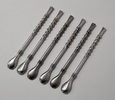 six cuillères en argent sont alignées sur une surface blanche