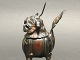 bronze statue of a dog with horns and a tail on a gray surface