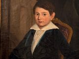 portrait of a young boy in a black coat sitting at a desk