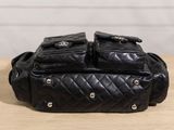 a black quilted bag with three compartments sitting on top of a wooden table