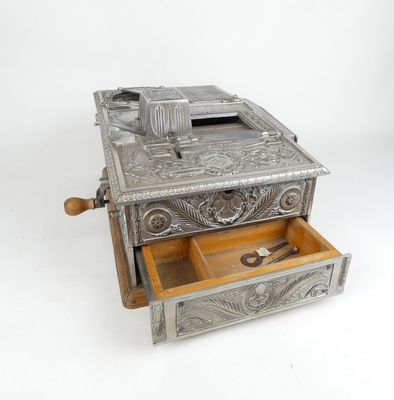 une caisse enregistreuse ancienne en métal argenté, avec un tiroir en bois et une paire de ciseaux