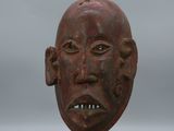 sculpture représentant le visage d'un homme, posée sur un socle, avec un ciel gris en arrière-plan