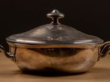 un pot en argent posé sur une table en bois, sur fond noir