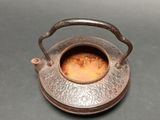 a small metal tea pot with a handle on a table