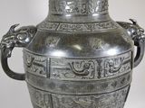 a silver vase with a dragon handle on a table