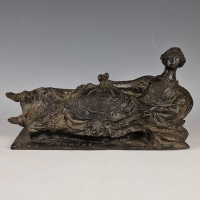 une statue antique en bronze représentant une femme allongée avec un chien