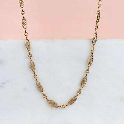 un gros plan d'un collier à chaîne en or posé sur une surface en marbre