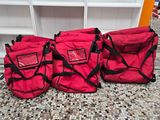 Trois sacs rouges sont alignés par terre devant une étagère
